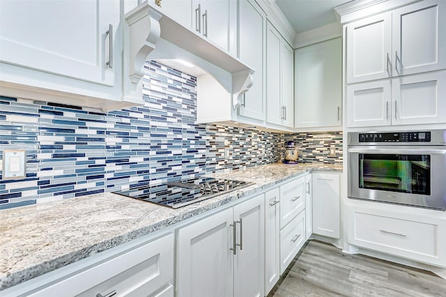 kitchen featuring white cabinets, oven, backsplash, gas stovetop, and light stone countertops