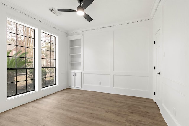 unfurnished room with built in shelves, ceiling fan, ornamental molding, and hardwood / wood-style floors