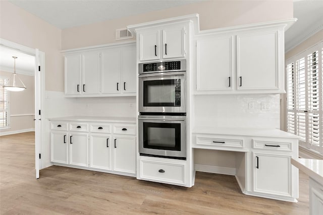 kitchen with pendant lighting, white cabinetry, ornamental molding, stainless steel double oven, and light wood-type flooring