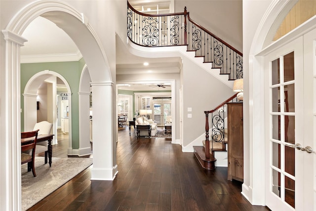 entryway with a towering ceiling, decorative columns, ornamental molding, ceiling fan, and dark wood-type flooring