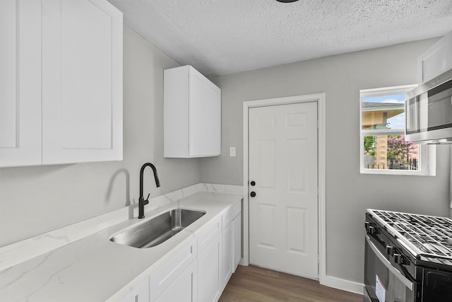 kitchen featuring black range with gas cooktop, sink, white cabinetry, a textured ceiling, and light hardwood / wood-style flooring