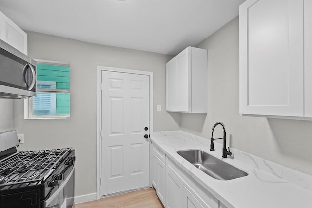 kitchen with sink, light stone counters, appliances with stainless steel finishes, light hardwood / wood-style floors, and white cabinets