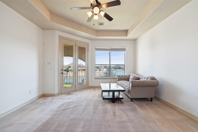 sitting room featuring a tray ceiling, light colored carpet, ceiling fan, and a water view