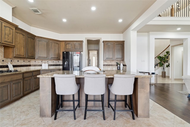 kitchen with a center island, a breakfast bar area, light stone counters, and black refrigerator with ice dispenser