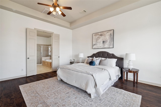 bedroom with dark wood-type flooring, ensuite bath, and a tray ceiling