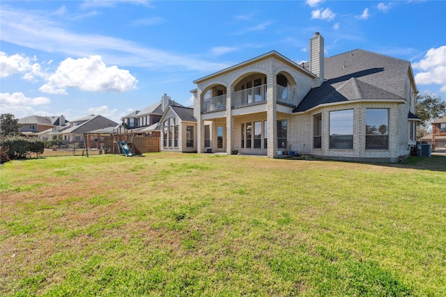 rear view of property featuring a playground, a balcony, and a lawn