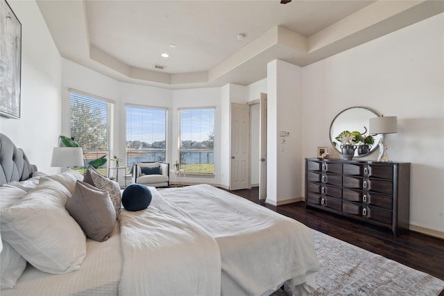 bedroom featuring dark hardwood / wood-style floors, a tray ceiling, and multiple windows