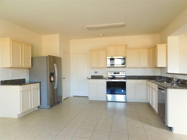 kitchen with light tile patterned floors, stainless steel appliances, sink, and dark stone counters