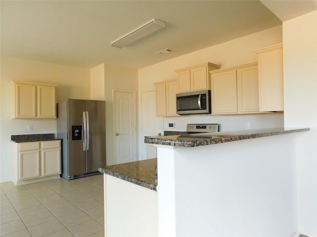 kitchen with light tile patterned floors, stainless steel appliances, dark stone counters, and kitchen peninsula