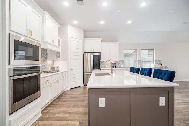 kitchen featuring sink, appliances with stainless steel finishes, a kitchen island with sink, decorative backsplash, and white cabinets