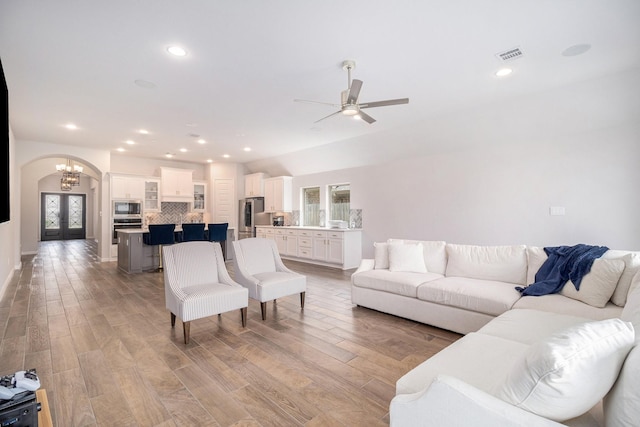 living room featuring ceiling fan with notable chandelier, vaulted ceiling, french doors, and light wood-type flooring