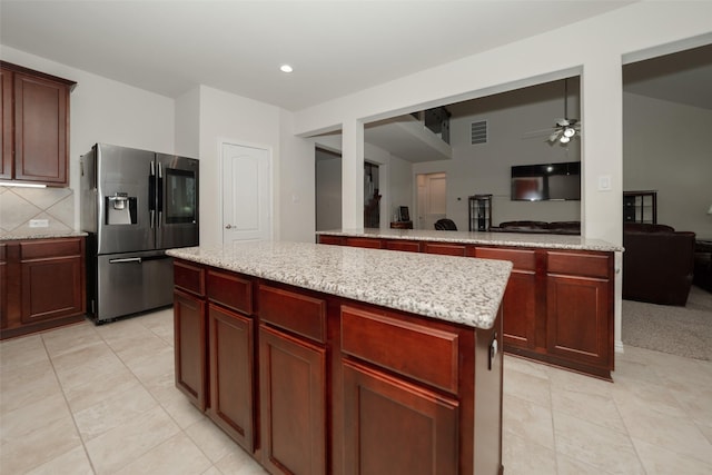 kitchen with ceiling fan, light stone counters, a kitchen island, stainless steel fridge with ice dispenser, and decorative backsplash