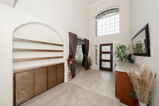 entryway with light tile patterned flooring, a towering ceiling, and crown molding