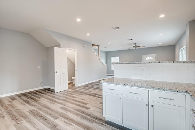 kitchen with white cabinetry, light wood-type flooring, ceiling fan, light stone countertops, and decorative backsplash