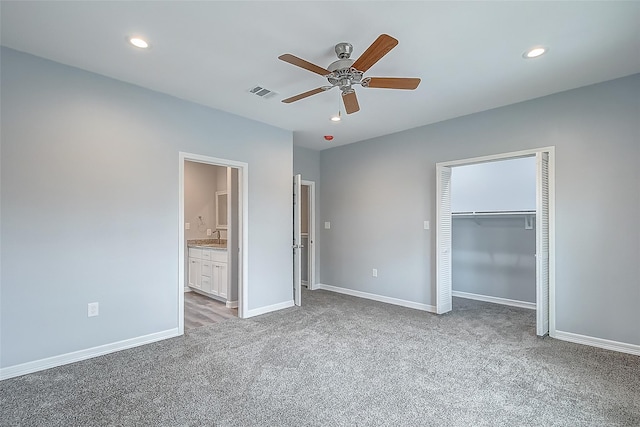 unfurnished bedroom with connected bathroom, sink, light colored carpet, ceiling fan, and a closet