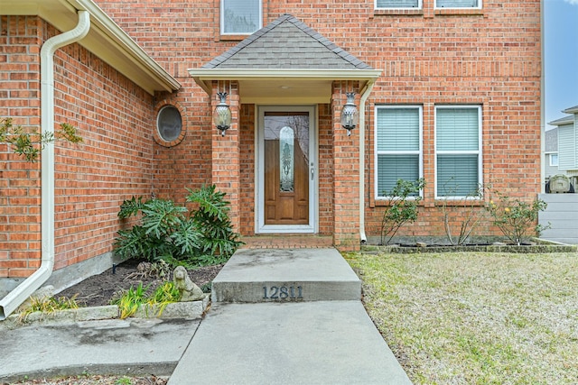 doorway to property featuring brick siding and a shingled roof