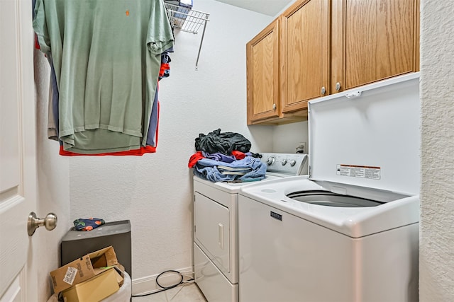 laundry room featuring washer and dryer, cabinet space, light tile patterned flooring, and a textured wall