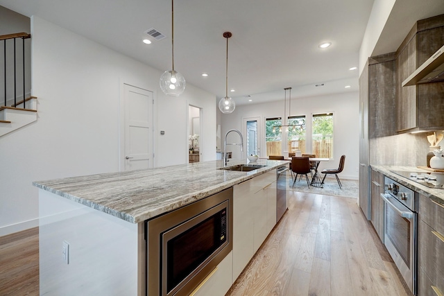 kitchen featuring sink, appliances with stainless steel finishes, pendant lighting, a large island, and light hardwood / wood-style floors