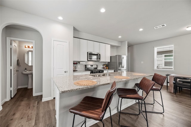 kitchen featuring a kitchen bar, light stone counters, white cabinetry, appliances with stainless steel finishes, and a kitchen island with sink