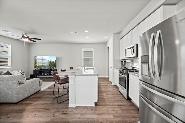 kitchen featuring stainless steel appliances, an island with sink, white cabinets, and a kitchen bar