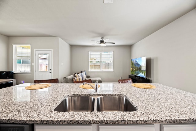 kitchen with ceiling fan, sink, an island with sink, and light stone counters