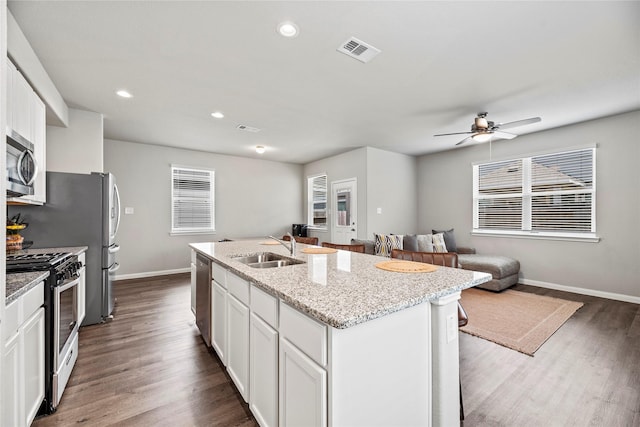 kitchen with sink, appliances with stainless steel finishes, a kitchen island with sink, light stone counters, and white cabinets