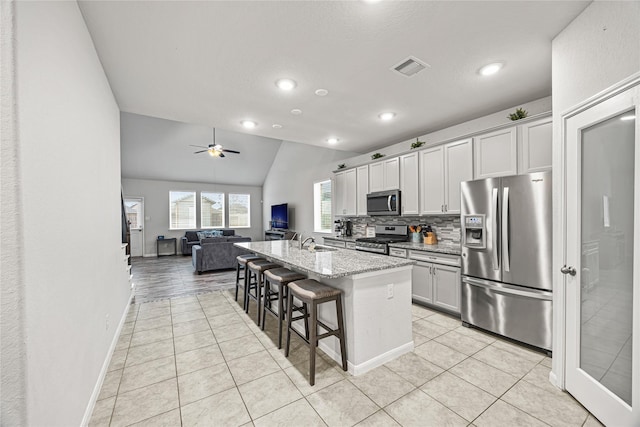 kitchen with a breakfast bar, vaulted ceiling, appliances with stainless steel finishes, an island with sink, and light stone countertops