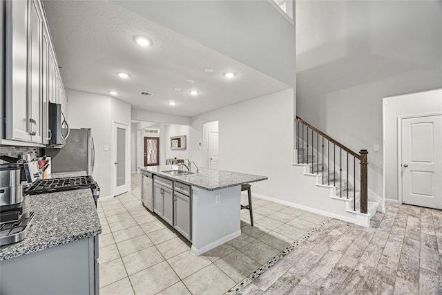 kitchen with gray cabinets, an island with sink, sink, dark stone countertops, and a kitchen bar