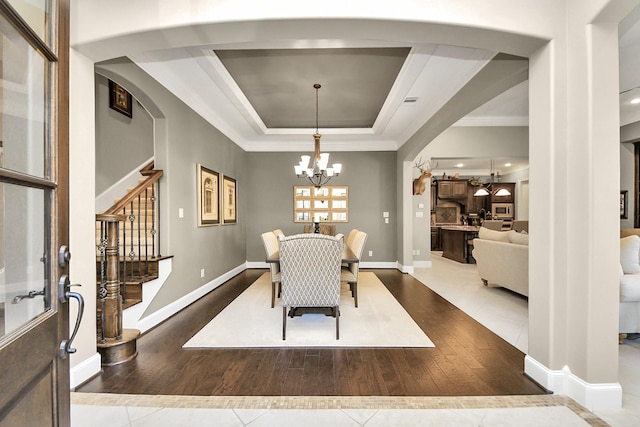 dining area featuring tile patterned flooring, arched walkways, a raised ceiling, and an inviting chandelier