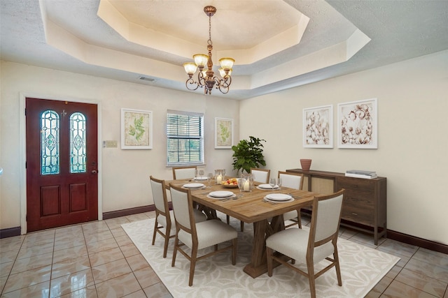 dining area with a tray ceiling, a chandelier, and light tile patterned flooring