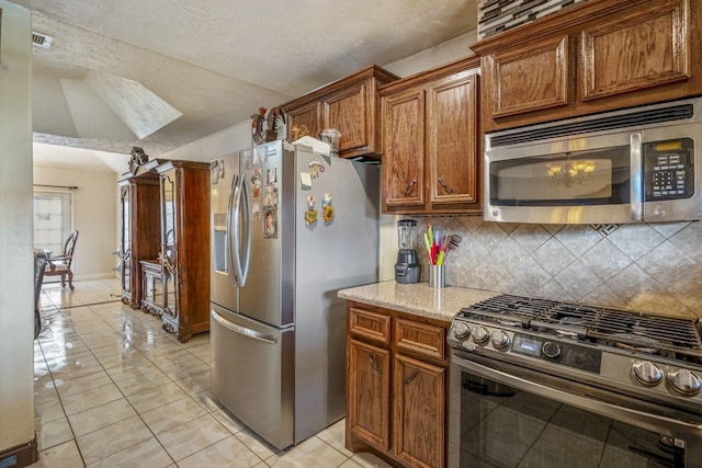 kitchen featuring appliances with stainless steel finishes, light stone countertops, light tile patterned floors, and backsplash