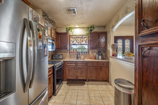 kitchen featuring sink, a textured ceiling, light tile patterned floors, appliances with stainless steel finishes, and decorative backsplash