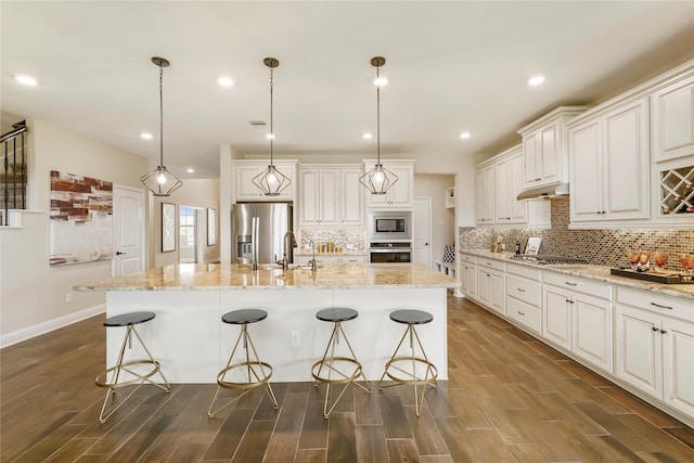 kitchen featuring a breakfast bar area, a center island with sink, pendant lighting, stainless steel appliances, and white cabinets