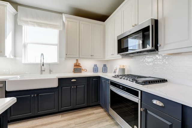 kitchen featuring tasteful backsplash, appliances with stainless steel finishes, light wood-style floors, white cabinetry, and a sink