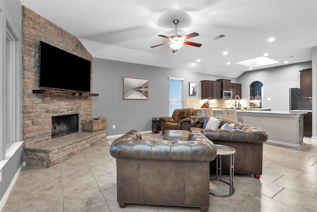 living room with light tile patterned flooring, ceiling fan, a fireplace, and lofted ceiling with skylight