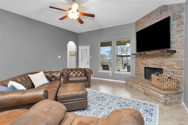 tiled living room featuring a stone fireplace and ceiling fan