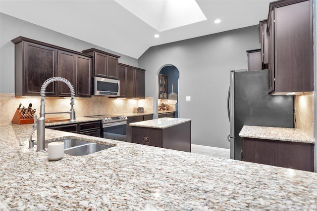 kitchen with sink, appliances with stainless steel finishes, backsplash, light stone countertops, and a kitchen island