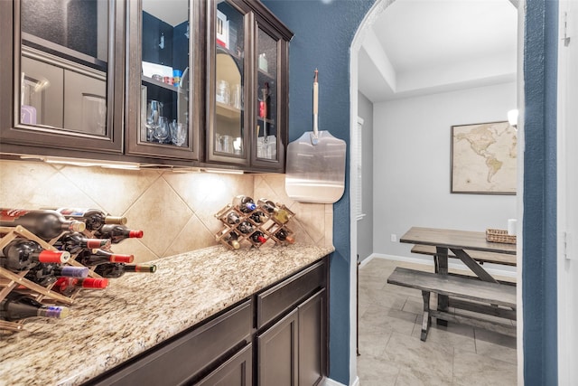 bar featuring dark brown cabinets, backsplash, and light stone counters