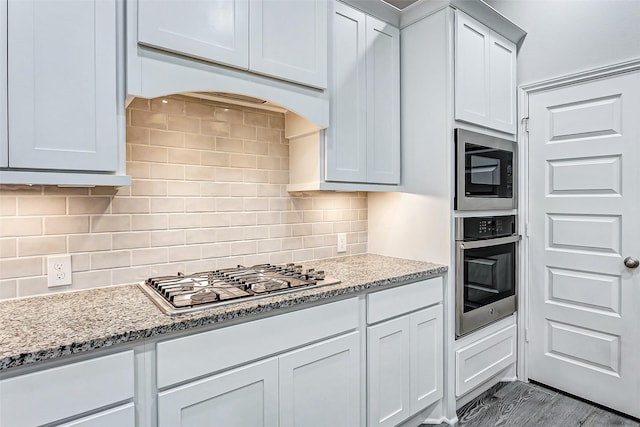 kitchen with stainless steel appliances, tasteful backsplash, light stone countertops, and white cabinets