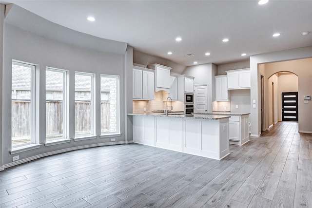 19723 Sandstone Bluff Way, Cypress, TX 77433 - kitchen with a sink, light stone countertops, a peninsula, white cabinets, and arched walkways