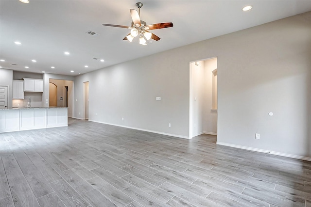 unfurnished living room featuring ceiling fan, sink, and light wood-type flooring