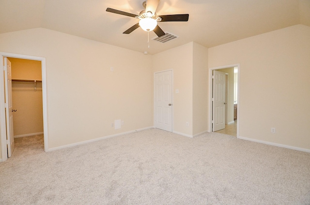 unfurnished bedroom featuring lofted ceiling, a walk in closet, light colored carpet, ceiling fan, and a closet