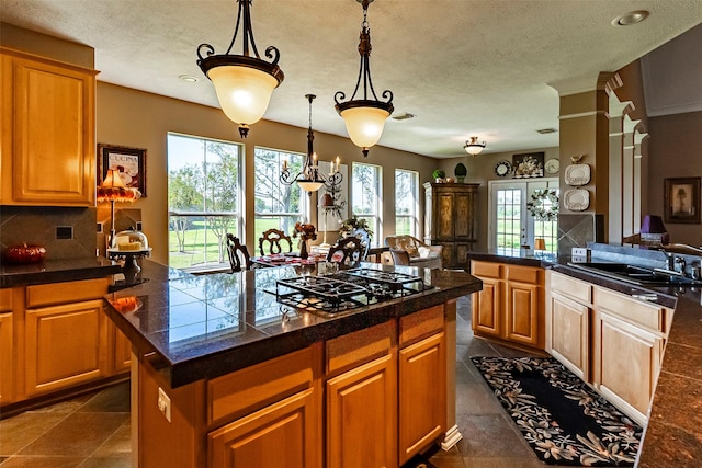 kitchen with pendant lighting, sink, backsplash, stainless steel gas cooktop, and a kitchen island