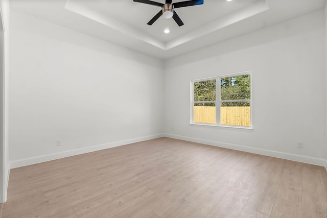 empty room with a raised ceiling, ceiling fan, and light hardwood / wood-style flooring