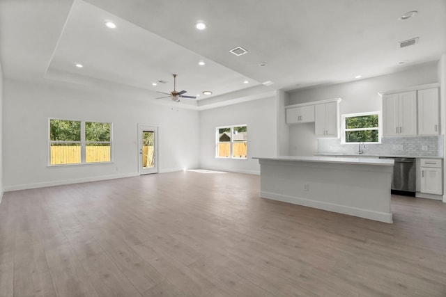 unfurnished living room featuring ceiling fan, sink, a tray ceiling, and light hardwood / wood-style floors