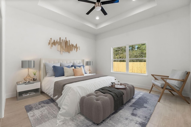 bedroom featuring ceiling fan, a raised ceiling, and light hardwood / wood-style flooring