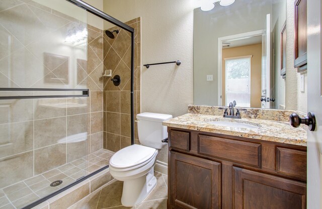 bathroom featuring tile patterned flooring, vanity, an enclosed shower, and toilet