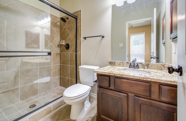 bathroom with a textured wall, toilet, vanity, tile patterned floors, and a stall shower