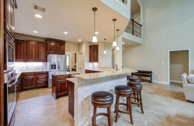 kitchen with appliances with stainless steel finishes, kitchen peninsula, pendant lighting, light stone countertops, and decorative backsplash