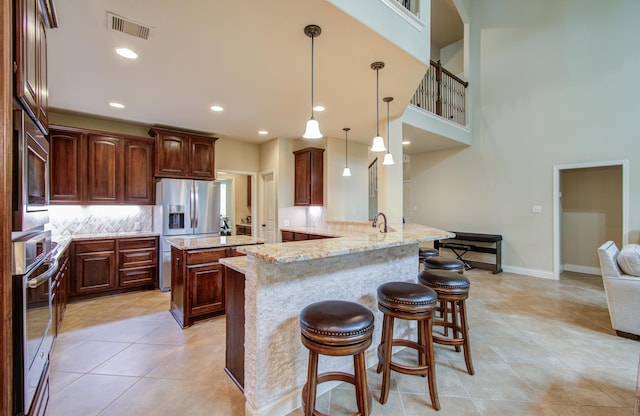 kitchen featuring light stone counters, a breakfast bar, stainless steel appliances, visible vents, and a peninsula